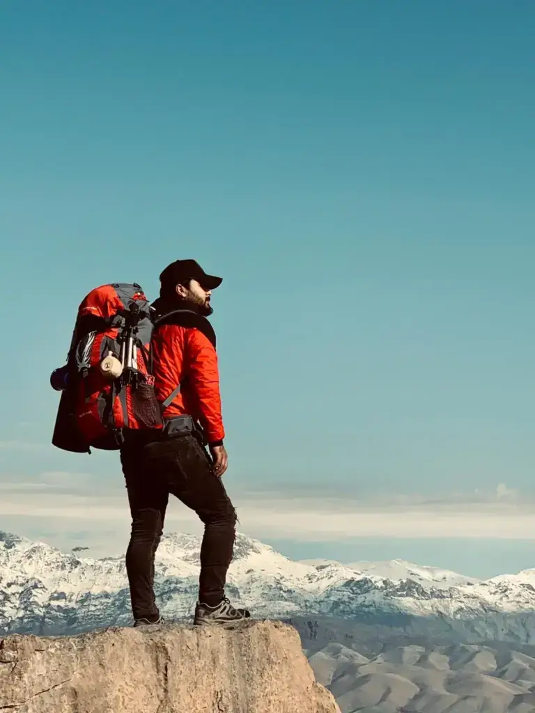 Traveler standing on a mountain cliff with a backpack, overlooking snow-covered peaks — symbolizing adventure, exploration, and the spirit of travel in India.